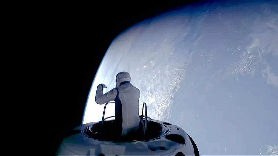 A person wearing a spacesuit stands at the hatch of a spacecraft, looking at Earth from space.