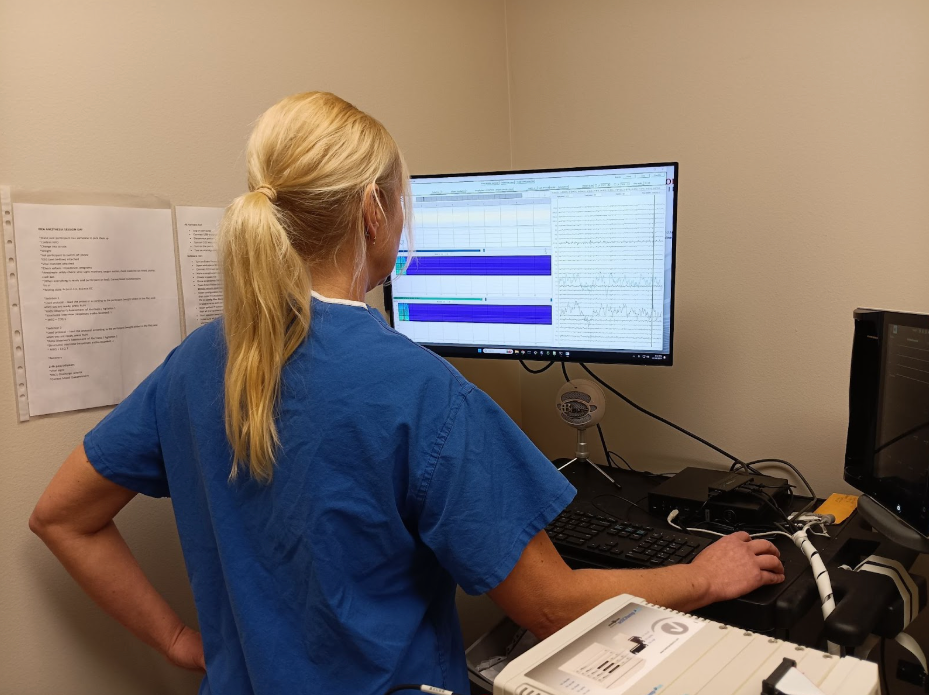 Inside the emerging world of anesthesia "dream therapy" 2 A person in blue scrubs analyzes data on a computer monitor in a medical setting.