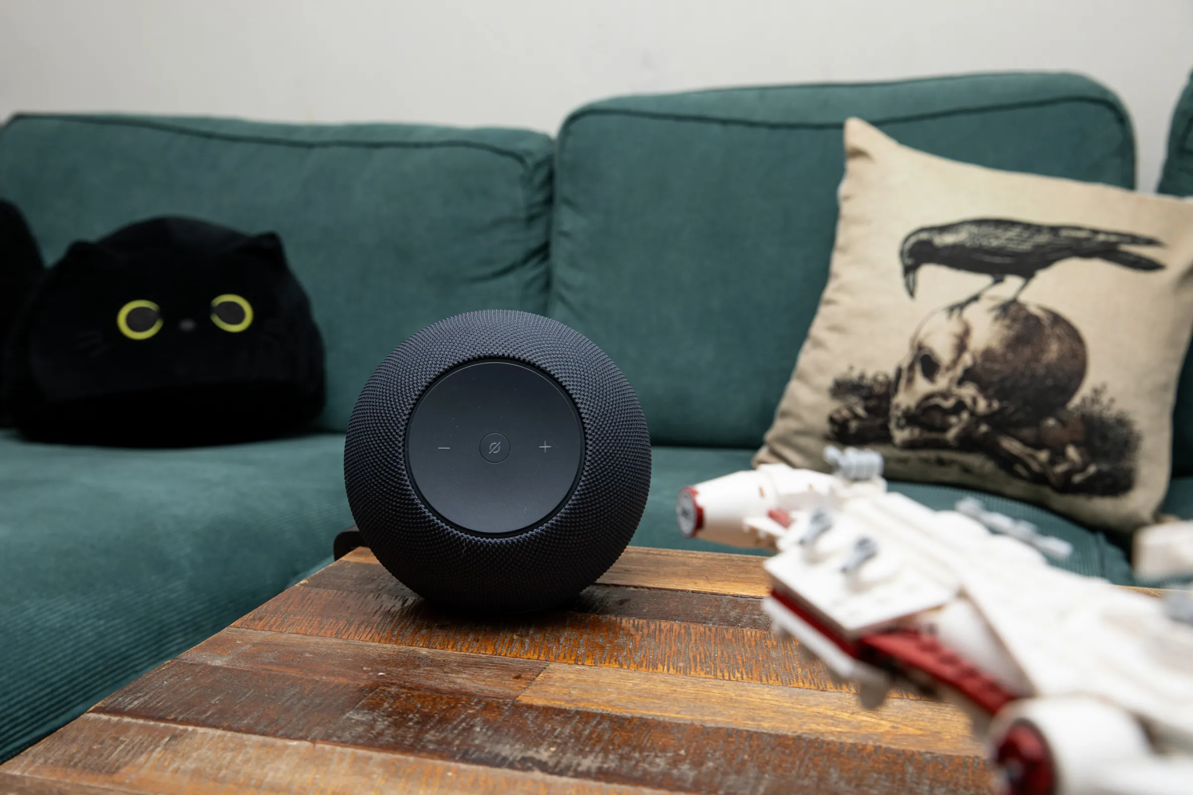 Amazon Echo Studio on a wooden coffee table in front of a green sofa with a Lego Star Wars ship in the foreground.