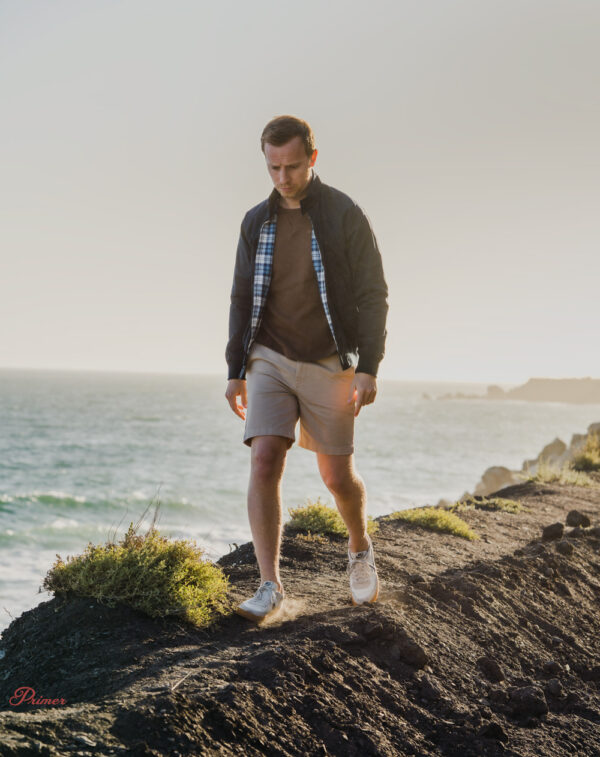 a man wearing a harrington jacket over a sweater, with shorts and sneakers