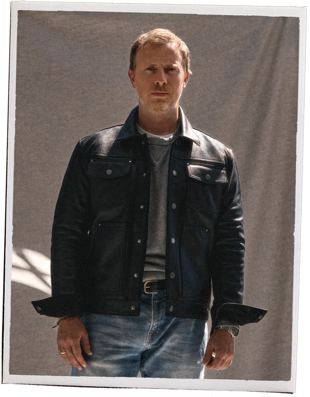 a man wearing a black leather jacket layered over a sweatshirt, jeans, and boots