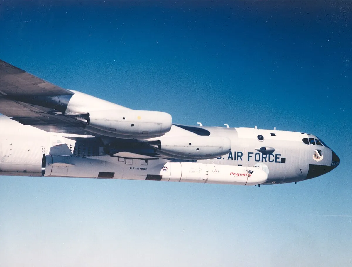 A US Air Force plane with a large missile underneath it flies in a clear blue sky.