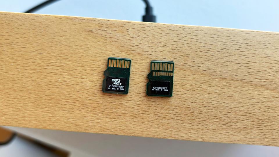 A standard UHS-I microSD card and an SD Express card rest face down on a brown wooden board, showing how the latter includes a second row of pins to improve performance.